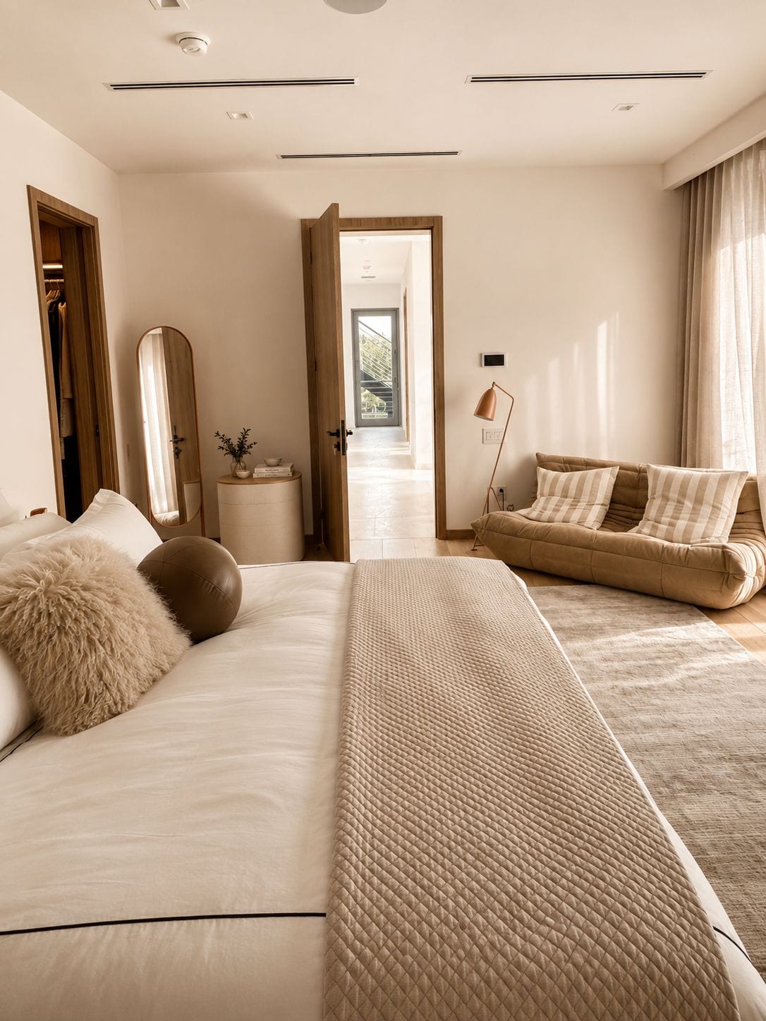The primary suite — a quilted cream bed, a low striped lounge by the window