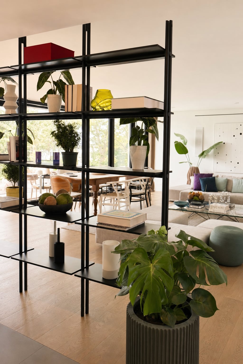 A black open steel shelving unit dividing the dining area from the living room, styled with books and ceramics