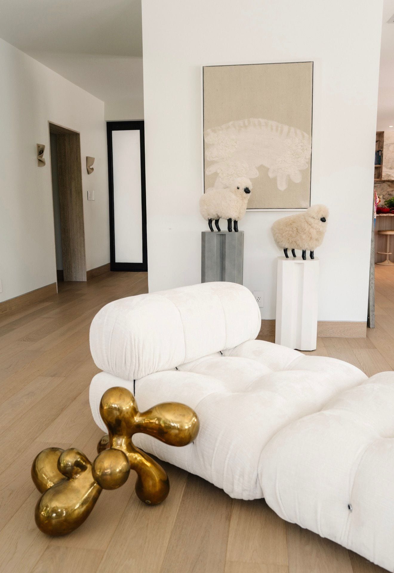 A styled corner — a tufted sofa, a brass sculpture on pale oak, art on a quiet wall