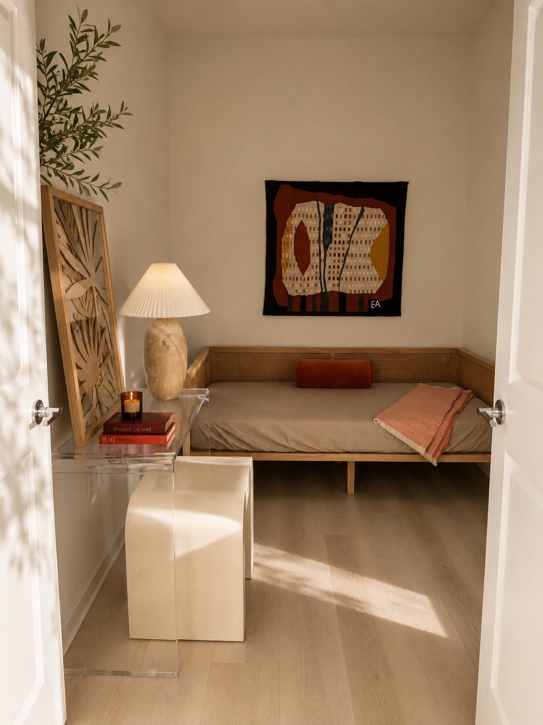 A flex nook — a cane daybed with a terracotta bolster, a sculptural table lamp, woven wall art in warm earth tones