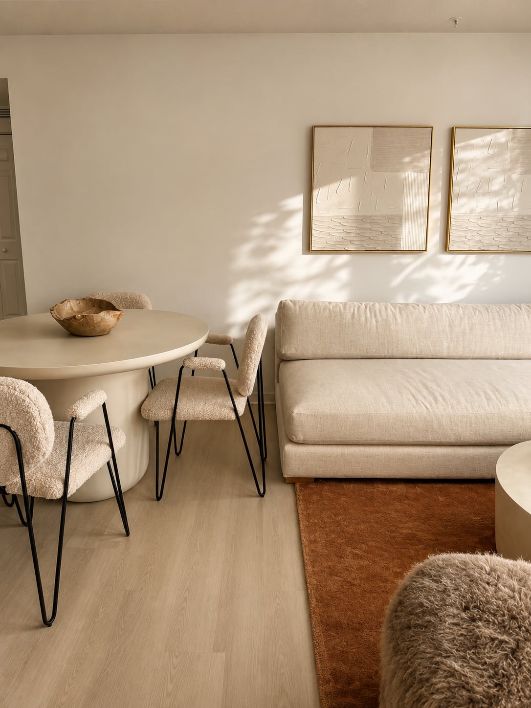 A detail of the living and dining area — bouclé dining chairs, textured plaster art, dappled light across the wall